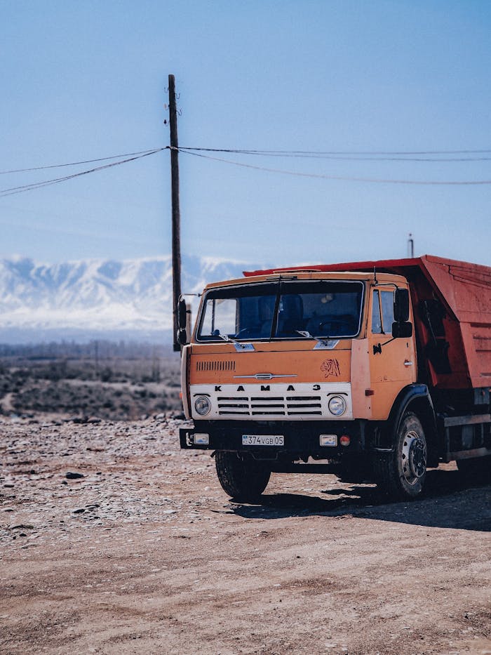 A classic Kamaz truck parked on a dirt road with mountains in the background.